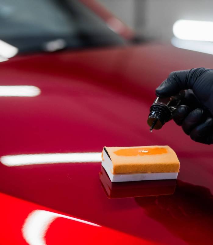 Close-up of a man hand dripping liquid coating on a sponge applicator on a car bonnet. Preparing for applying special coating on a car surface